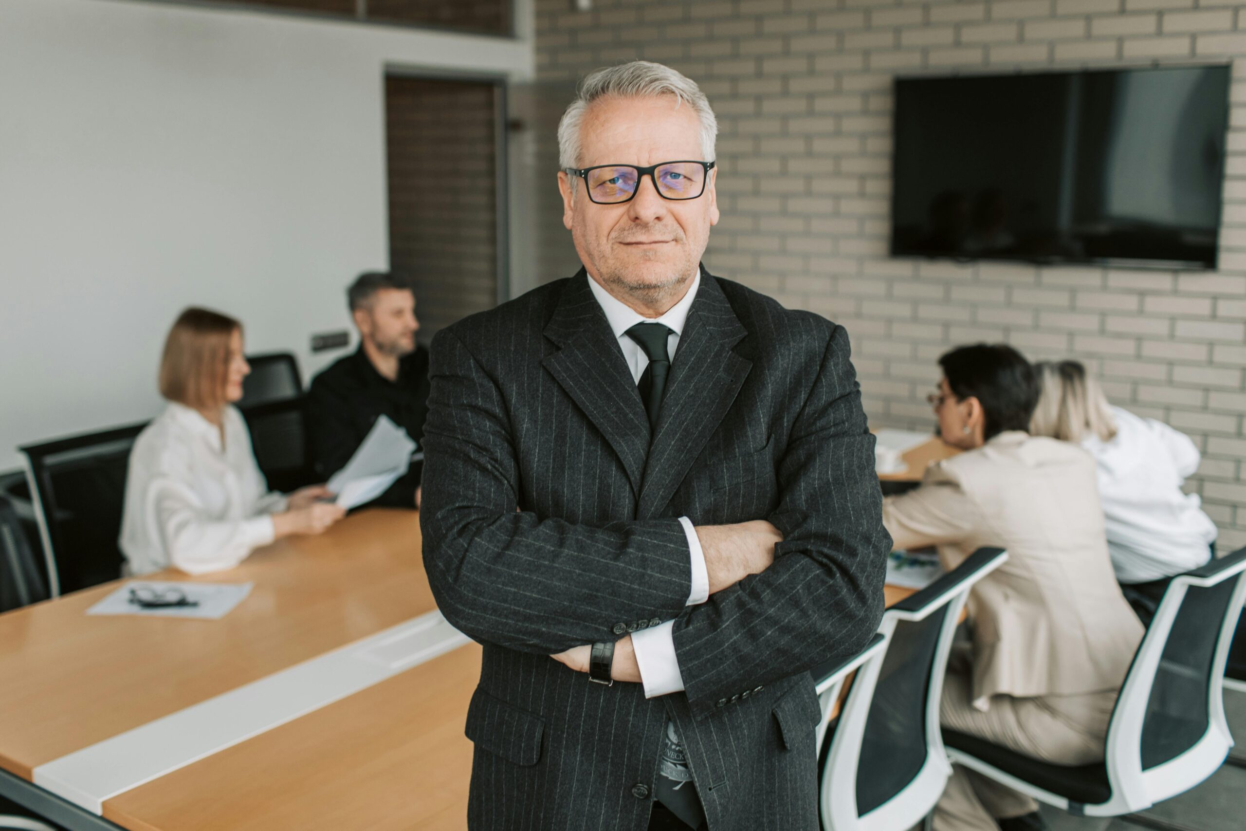 Senior businessman standing confidently with colleagues in a modern office setting.